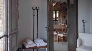 Ein Zimmer mit einer Holztür, die in einen Essbereich führt. Auf einem Regal liegen Handtücher gestapelt und ein weißer Stuhl ist zu sehen.
