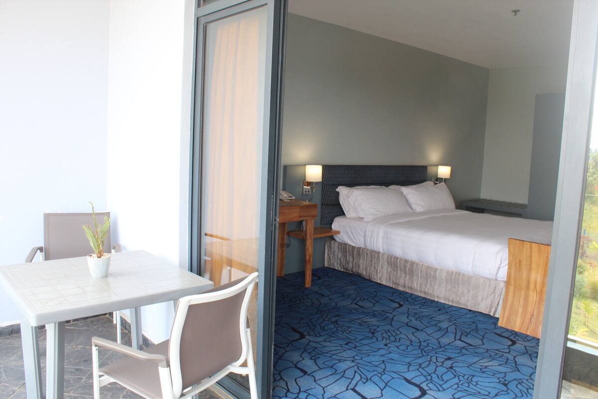 Ein Hotelzimmer mit Bett, Nachttisch, Lampe, Stuhl und einem kleinen Tisch mit Pflanze.