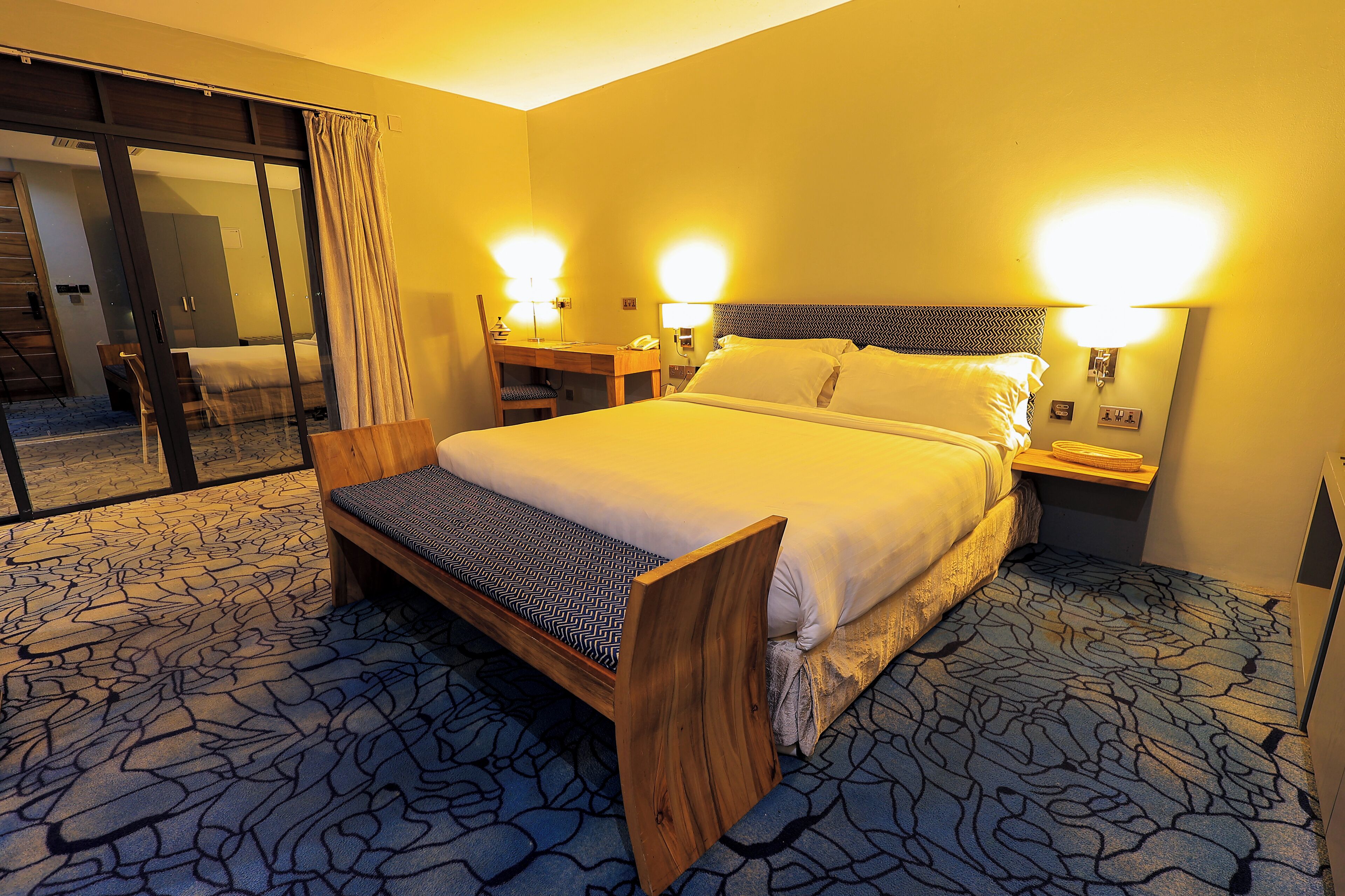 A hotel room with a bed, bedside tables, a desk, and a chair.