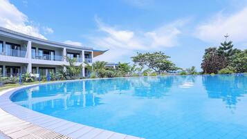 A modern hotel with a large swimming pool, a covered outdoor area, and lush greenery.