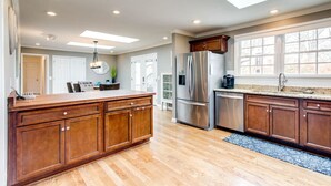 A spacious kitchen with wooden cabinets, a stainless steel refrigerator, and a large island. - Private Hot Tub, Porch Fireplace, Large Yard (Franklin)