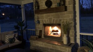 A stone fireplace with a fire, surrounded by shelves with decorative items, a sofa, and potted plants. - Private Hot Tub, Porch Fireplace, Large Yard (Franklin)