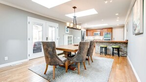A modern kitchen with a central island, wooden flooring, and a dining area with a table and chairs. - Private Hot Tub, Porch Fireplace, Large Yard (Franklin)
