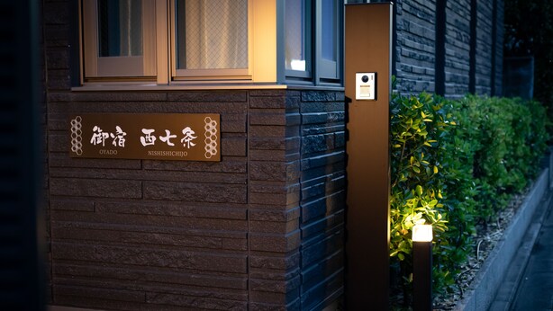 A building facade with a sign indicating "NISHISHICHIJI" and a small illuminated sign on the right. - Oyado Nishishichijo (Kyoto)