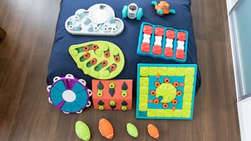 A variety of children's toys and educational materials arranged on a dark blue mat on a wooden floor.