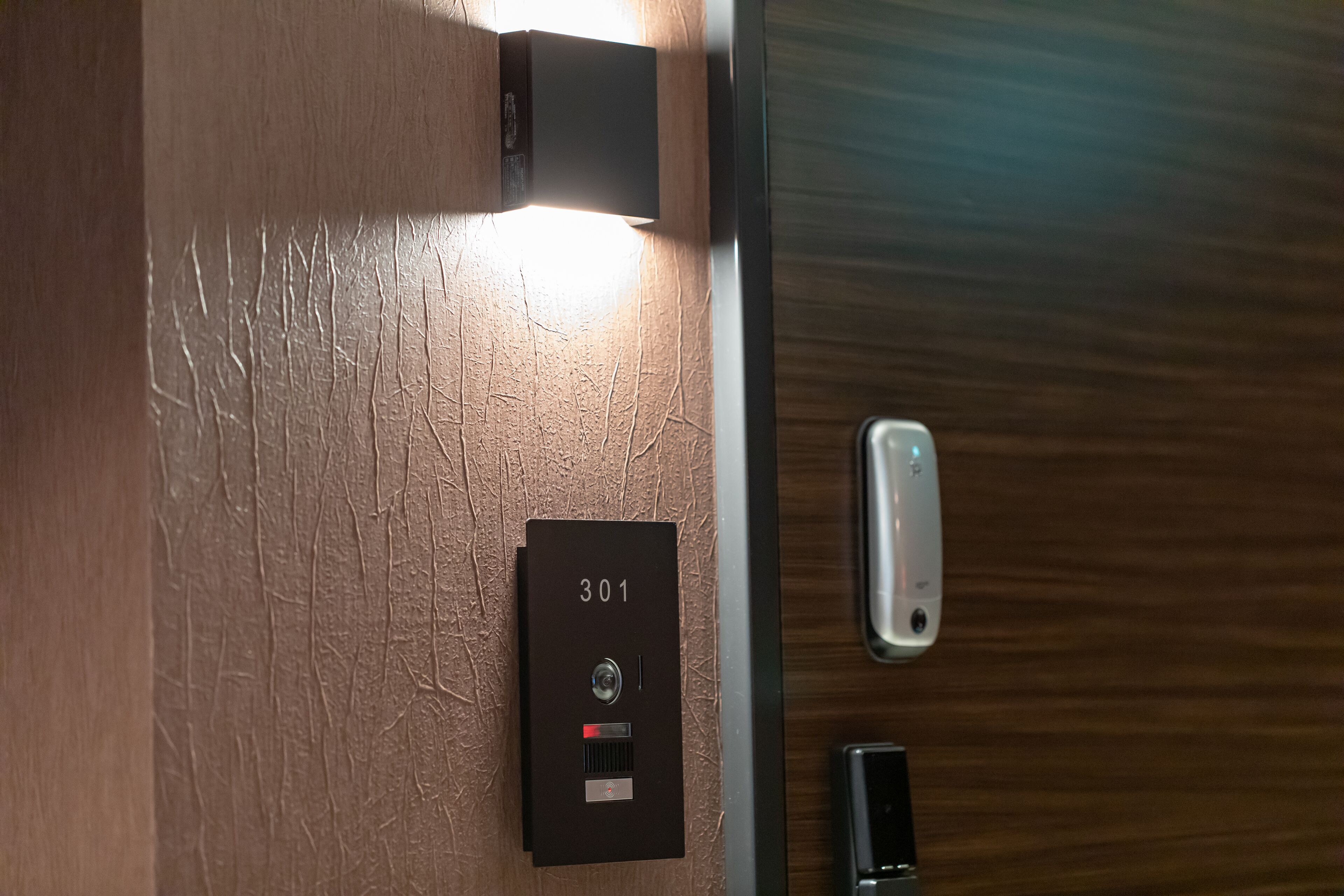 Een detailopname van een hotelkamer, met een houten wand, een deur met metalen handvat en een intercominstallatie met het nummer 301.