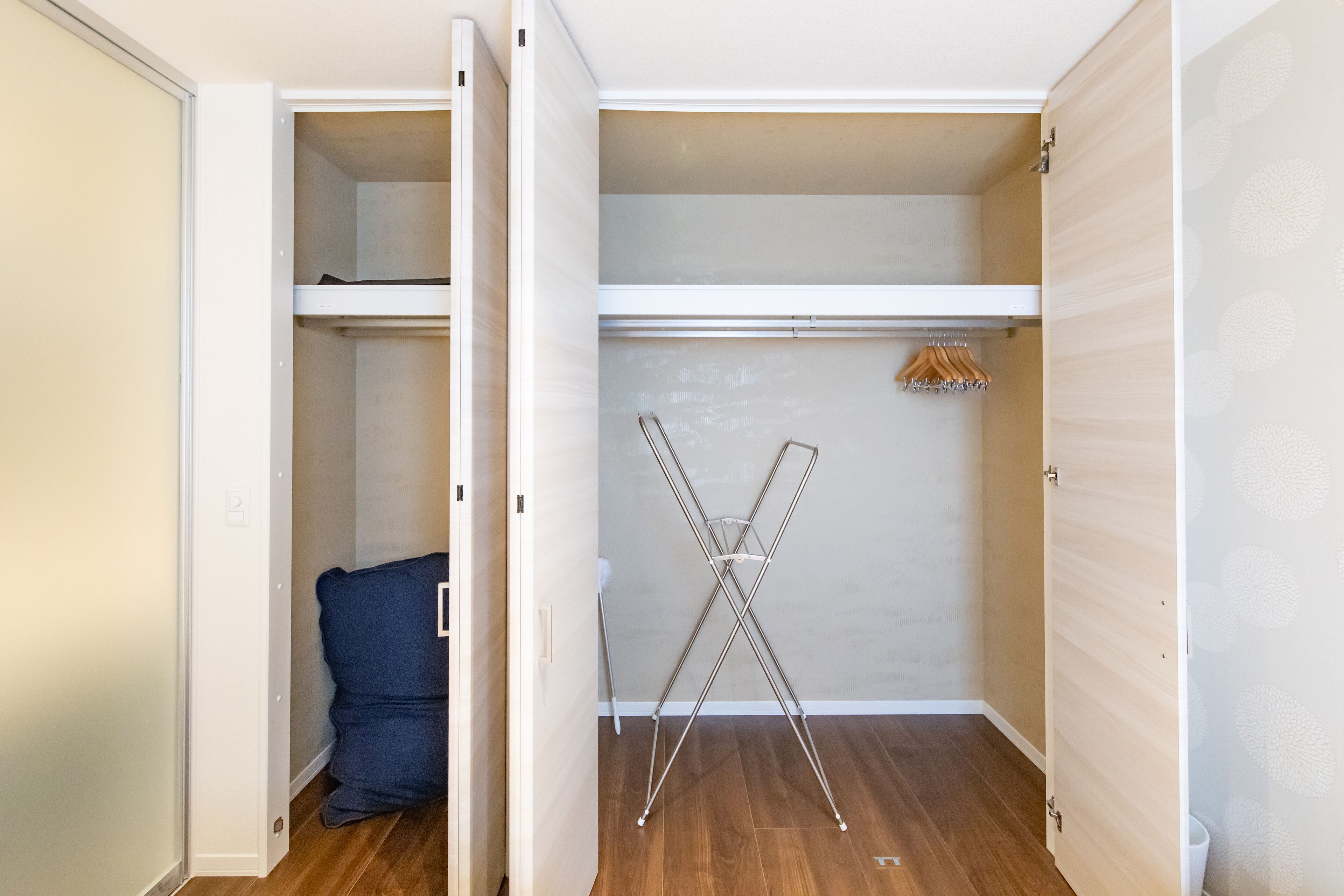 Un armario abierto con barra para colgar, una silla plegable y una silla azul.