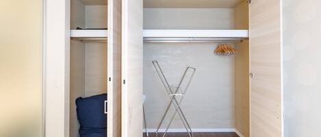Un armario abierto con barra para colgar, una silla plegable y una silla azul.