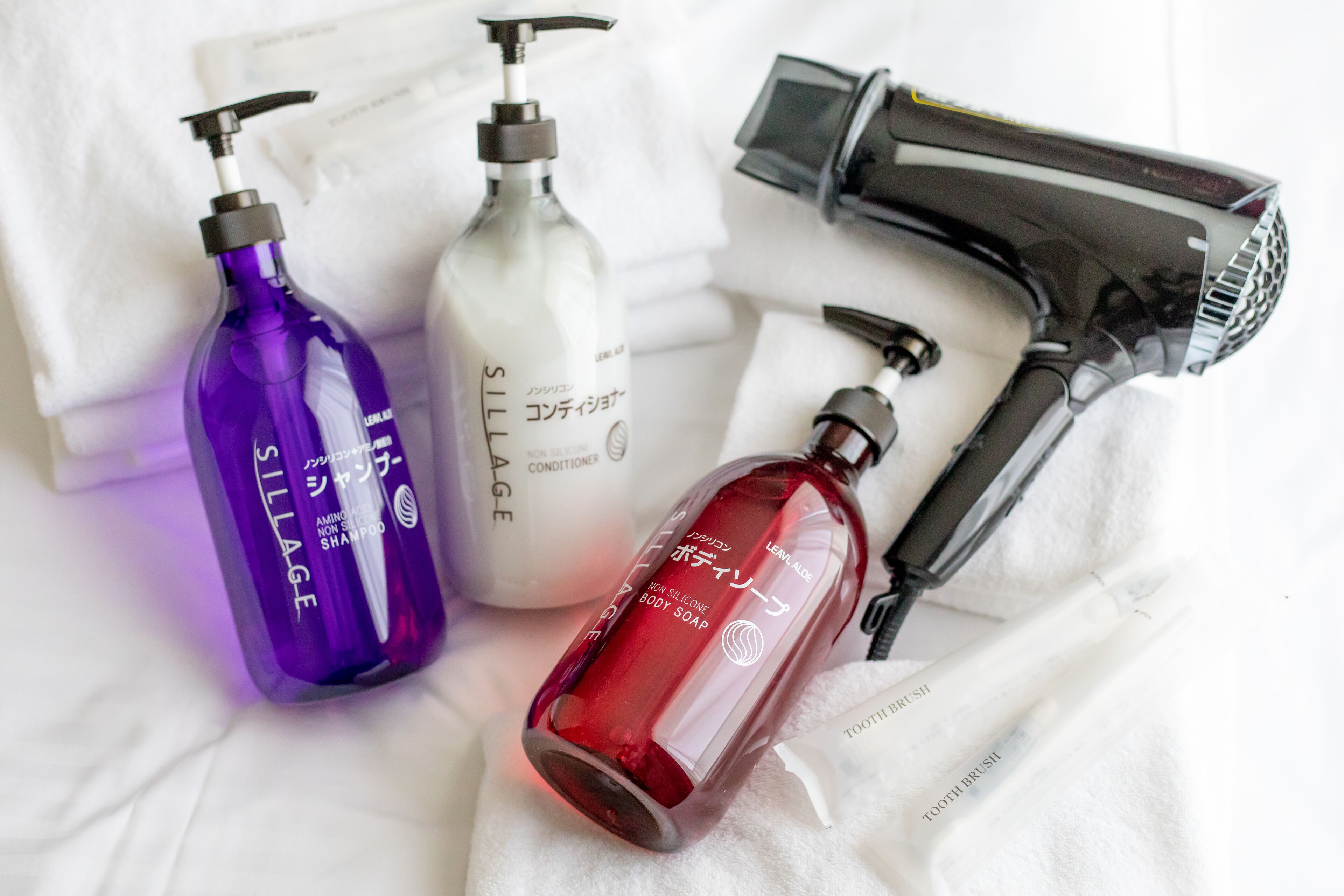 A hair dryer, three bottles of hair care products, and a toothbrush on a white towel.