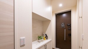 A hallway with a white countertop, a potted plant, a phone, and a door with a keypad and a map. - Oyado Nishishichijo (Kyoto)