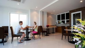 A modern dining area with tables and chairs, a kitchen area, and a large window. - LaXenia (Karon)