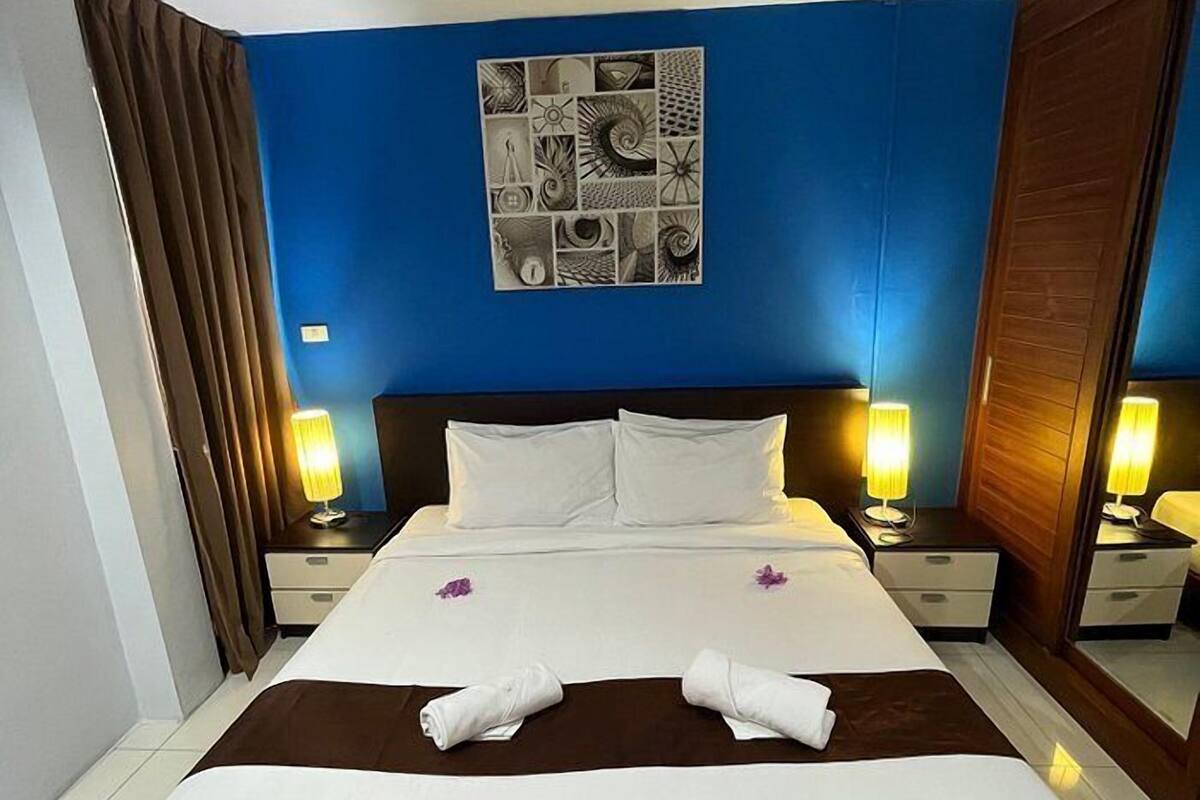 A hotel room with a large bed, two bedside tables with lamps, a blue accent wall, and a wall art piece.