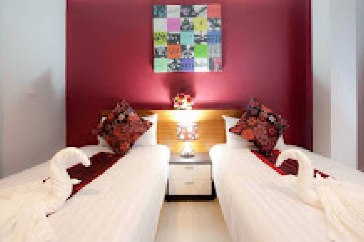A room with two beds, a nightstand, a lamp, and a colorful abstract painting on the wall.