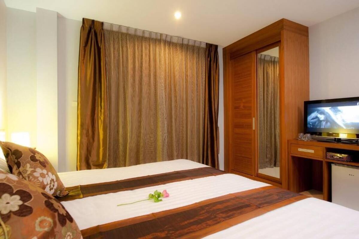 A hotel room with a bed, a television, a wooden wardrobe, and a mirror.