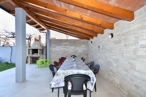 An outdoor patio with a long table, chairs, and a stone fireplace. - Apartment 2221/66969 (Istria - Medulin), 900m from the beach (Medulin)