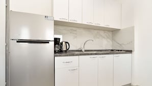 A kitchen with white cabinets, a stainless steel refrigerator, a sink, and a coffee maker.