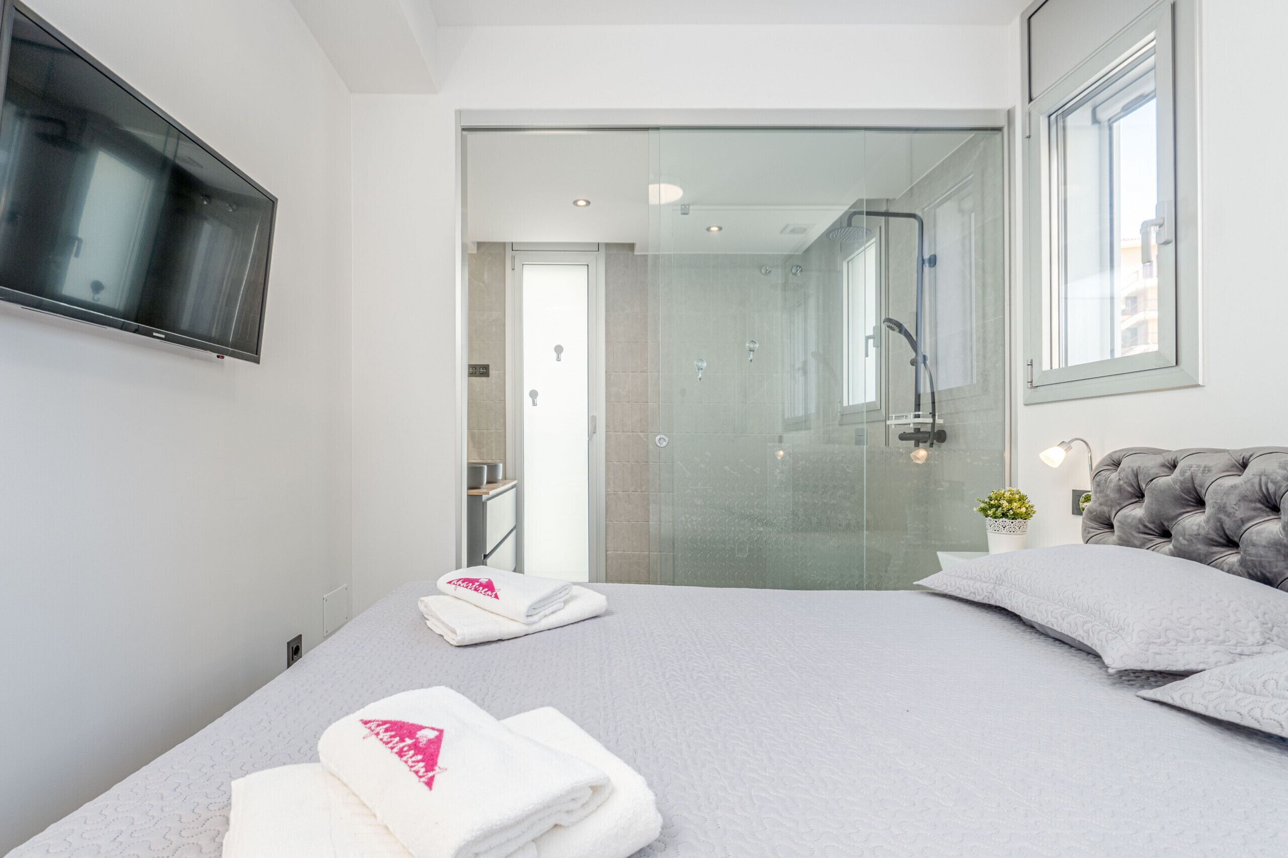 Ein modernes Hotelzimmer mit Bett, Fernseher, einer Duschkabine aus Glas und Blick auf die Stadt.