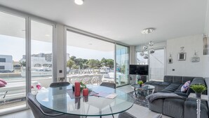 A modern living room with a glass table, grey sofa, and a balcony with a view of the city.