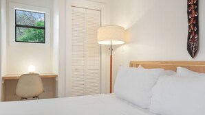 Et hotelværelse med en seng, et skrivebord, en stol, en lampe og udsigt til træer gennem et vindue.