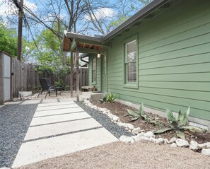 Una casa verde con un porche cubierto, un camino de grava y un pequeño jardín con plantas.