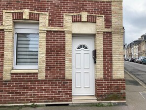 A red brick building with a white door and window, a small porch, and a mailbox.