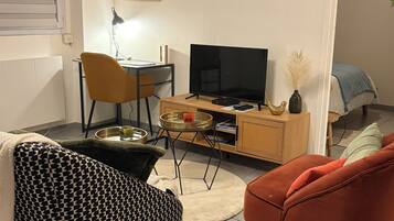 Een woonkamer met een bank, een rode stoel, een televisie, een salontafel en een kast.