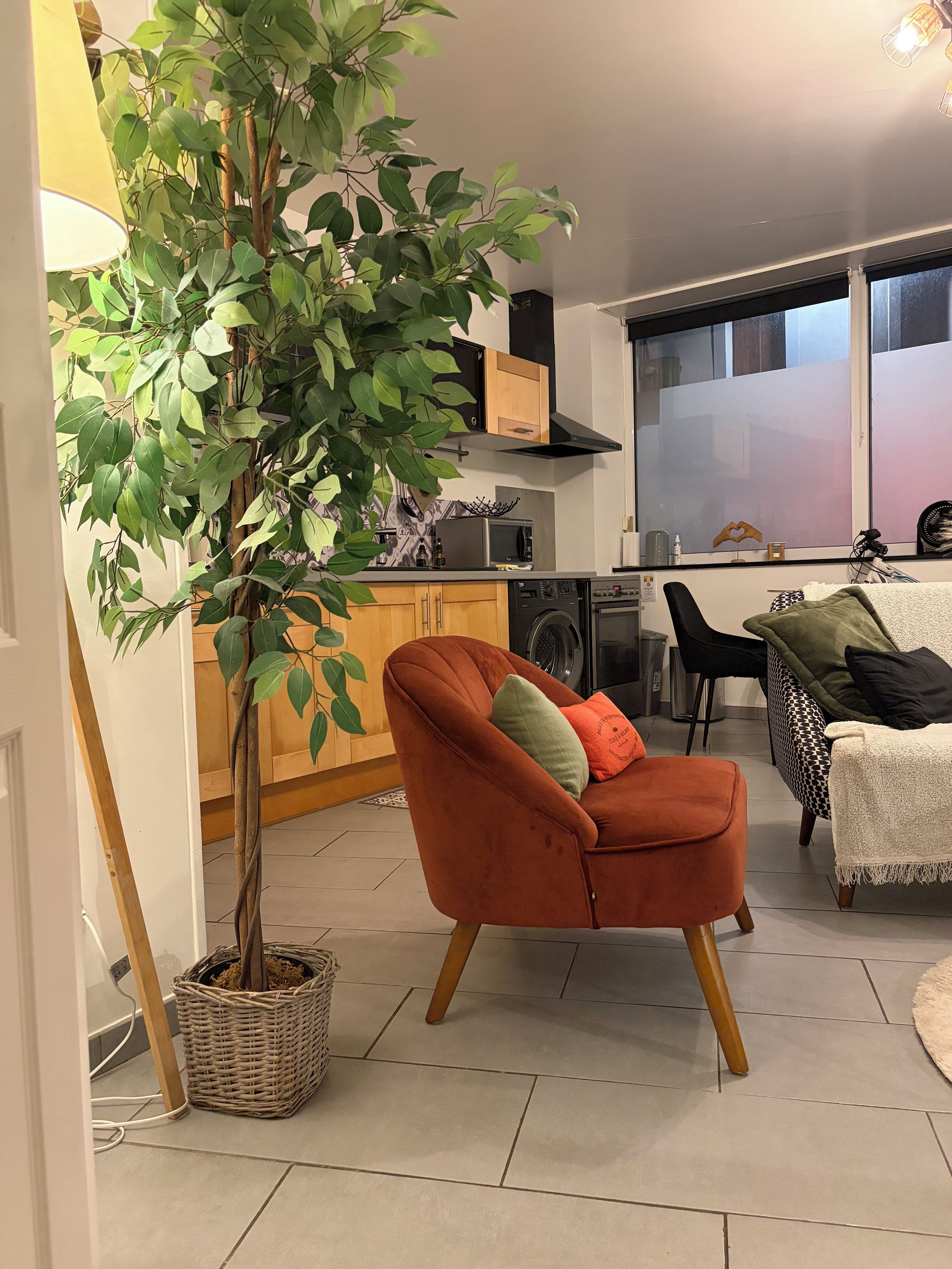 Een moderne woonkamer met een rode fauteuil, een kamerplant en een eethoek met een tafel en stoelen.
