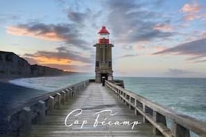A wooden pier leading to a lighthouse with a red top, overlooking a beach and ocean.