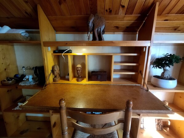 A wooden dining table with chairs, a shelf with busts, a potted plant, and a ceiling with wooden beams.