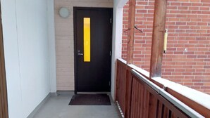 A narrow corridor with a black door, a wooden railing, and a brick wall. - Kuukkeli Sodankylä Apartments (Sodankyla)