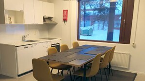 A compact kitchen with a dining area, a window with a view of a snowy outdoor scene, and a fire extinguisher on the wall. - Kuukkeli Sodankylä Apartments (Sodankyla)