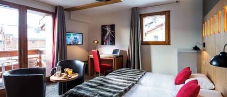 A hotel room with a bed, a desk, a chair, a small table with breakfast, and a TV.