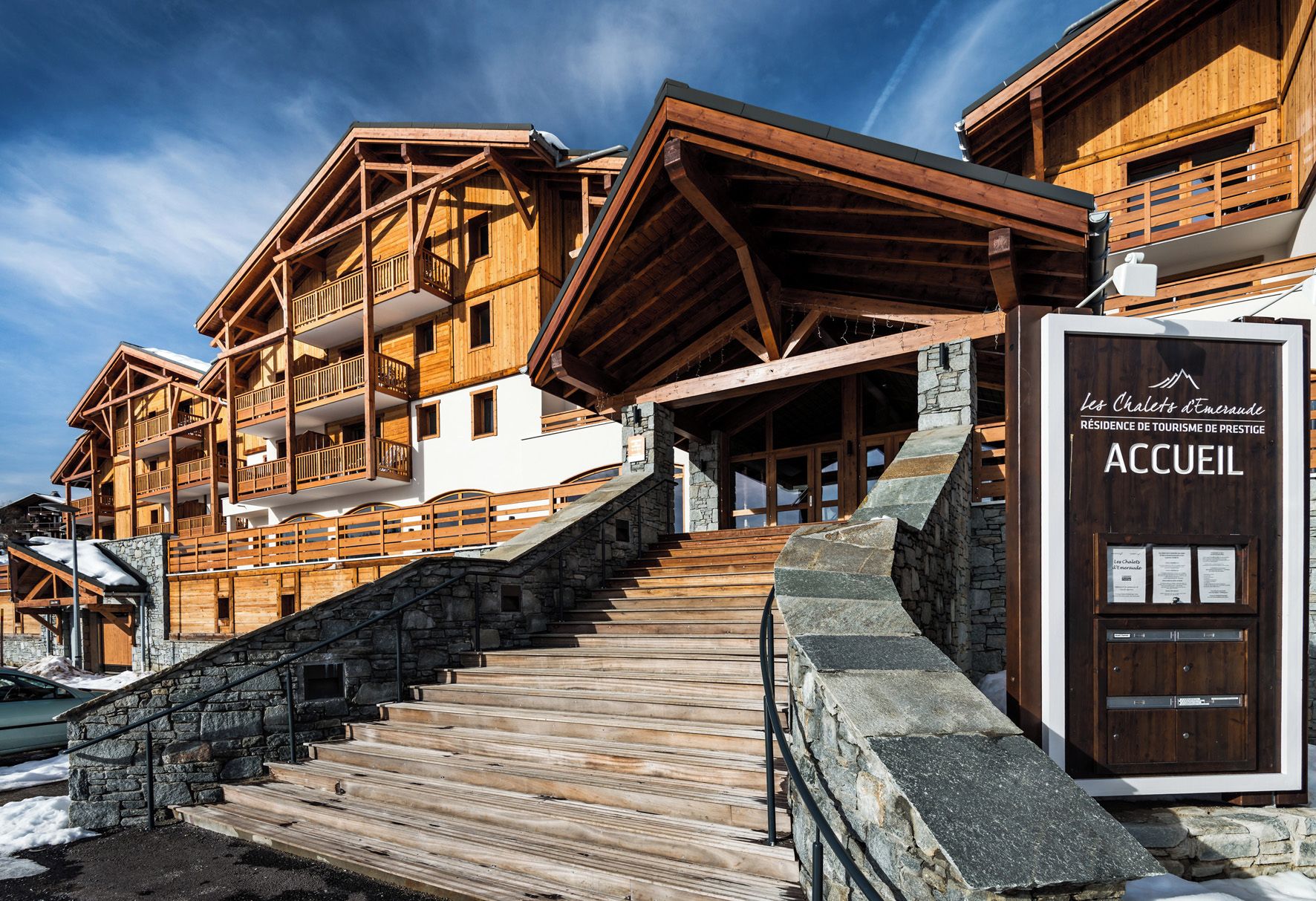 A wooden chalet-style building with a stone staircase leading to a wooden door labeled 'ACCUEIL.'