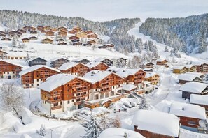 Un complejo turístico nevado con varias edificaciones de madera, una pista de esquí al fondo y un cielo despejado.