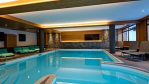 Una piscina interior con pared de piedra, vigas de madera y sillones de descanso.