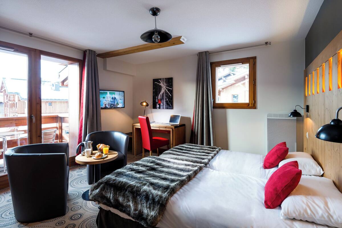 A hotel room with a bed, a desk, a chair, a small table with breakfast, and a TV.