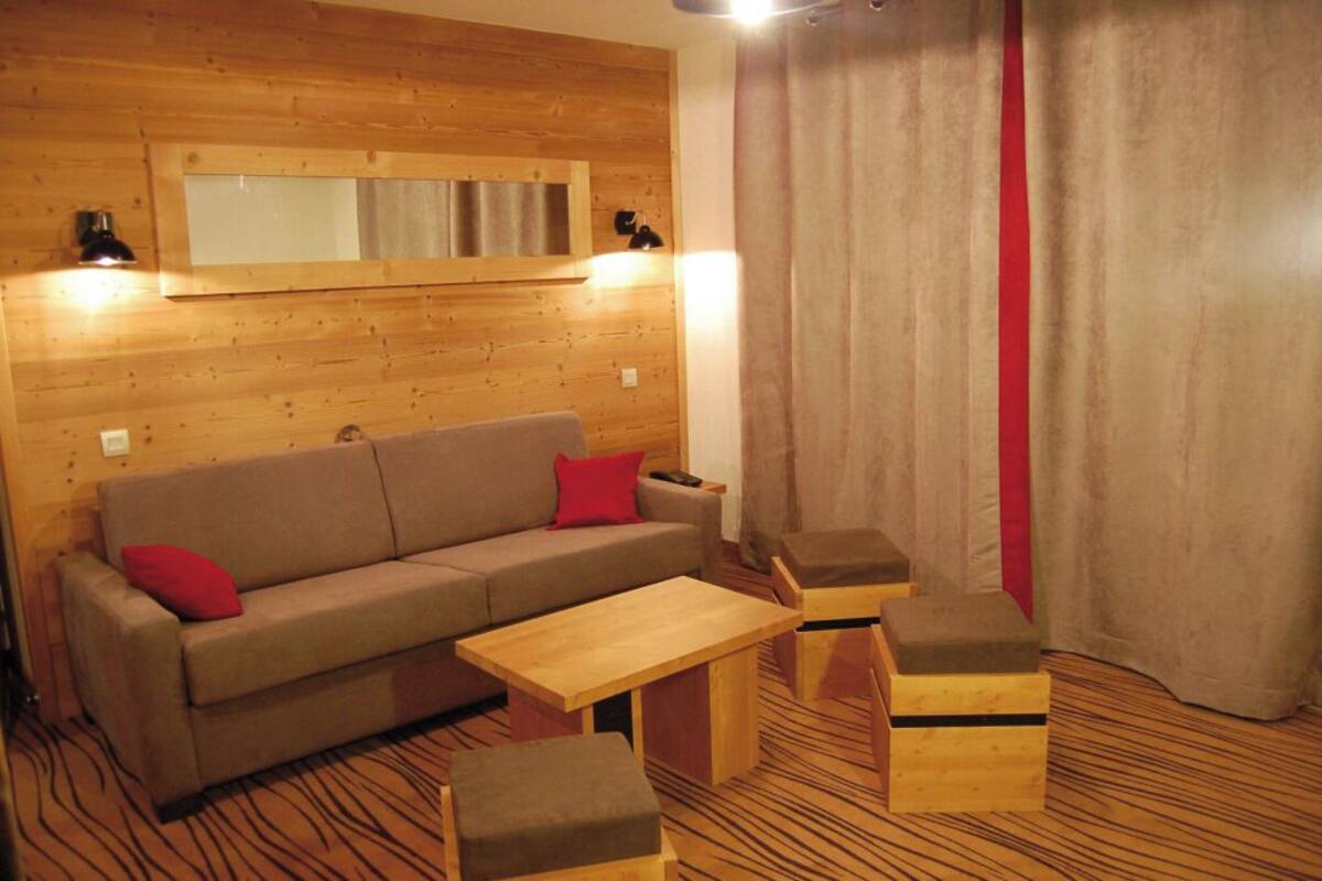 A wooden-paneled room with a sofa, two ottomans, a small table, and a mirror on the wall.