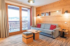 Una habitación con sofá, una mesita, un banco de madera, un espejo y vistas a través de un ventanal corredera.