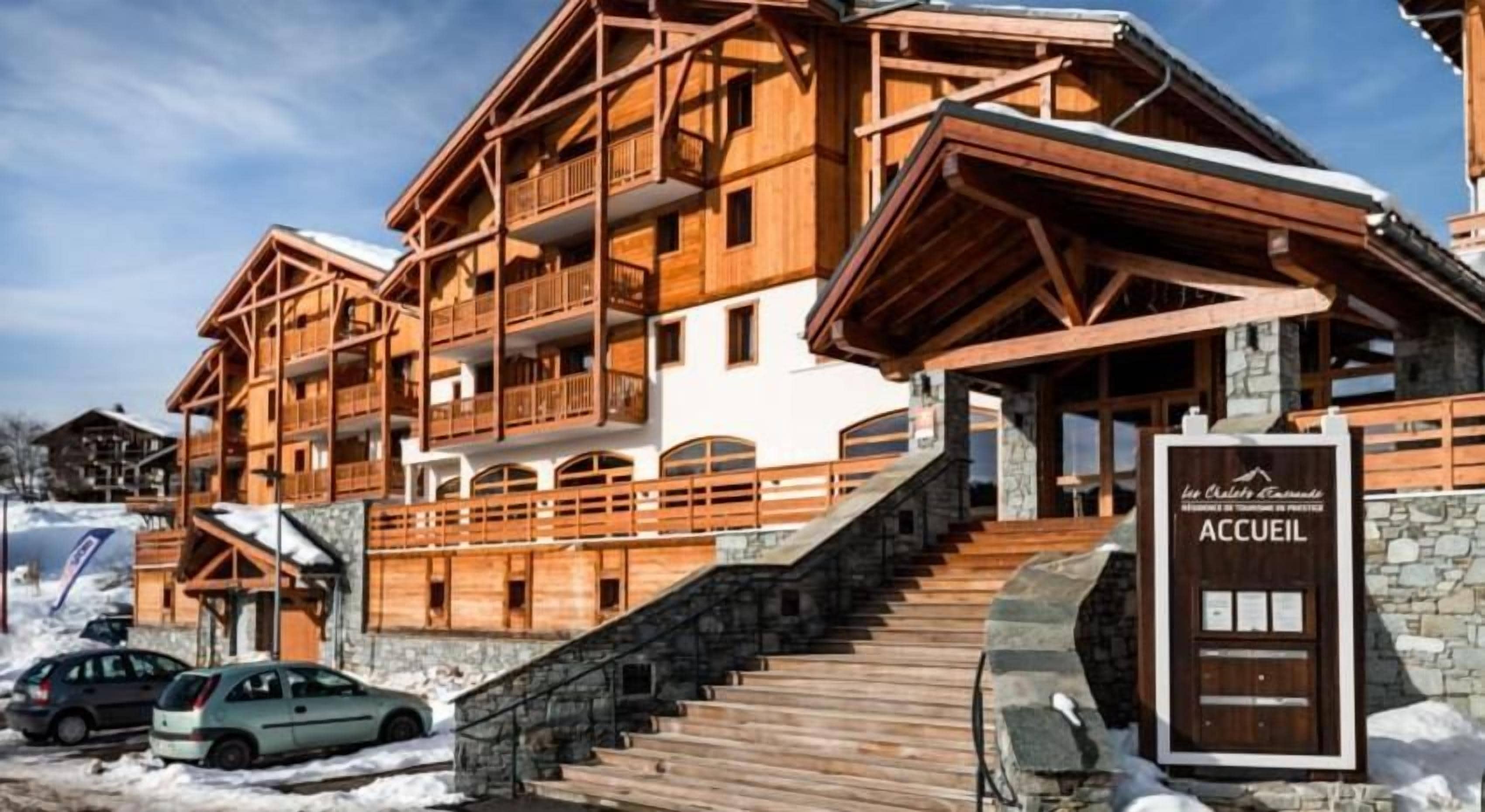 Un chalet en bois à plusieurs étages, doté de balcons, d’un escalier en pierre et d’une enseigne sur laquelle on peut lire « ACCUEIL ».