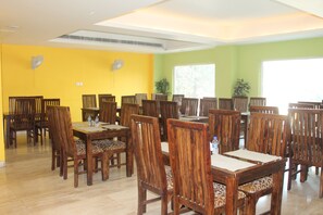 A dining area with multiple wooden tables and chairs, a yellow wall, and a green wall. - THE J K Hotel C R Park (New Delhi)