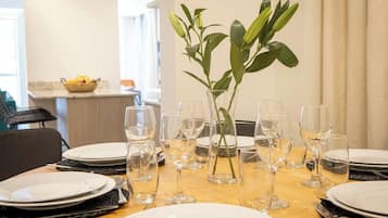 A dining table set with white plates, clear wine glasses, and a vase with green leaves.