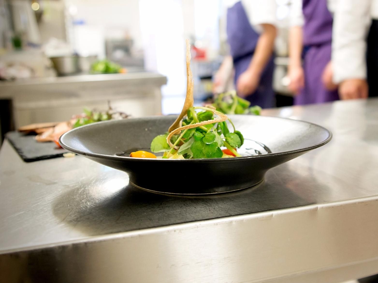 A black bowl on a stainless steel counter with a salad.