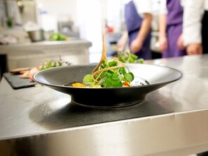 A black bowl on a stainless steel counter with a salad. - Logis Hôtel de France Restaurant le Lucullus (Montmorillon)