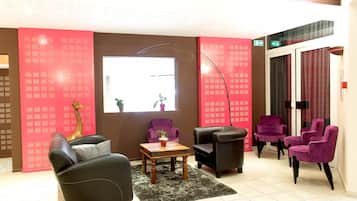 Eine Lobby mit einer Couch, Sesseln, einem Tisch, einer Stehlampe und einem großen Fenster.