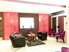 A lobby with a sofa, armchairs, a table, a floor lamp, and a large window. - Logis Hôtel de France Restaurant le Lucullus (Montmorillon)