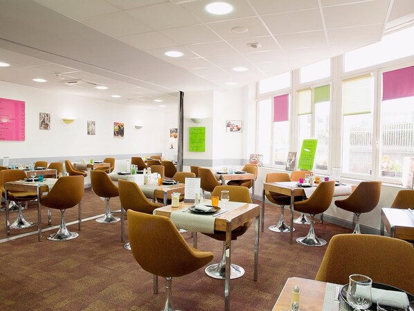 A dining area with tables and chairs, a carpeted floor, and a view through large windows.