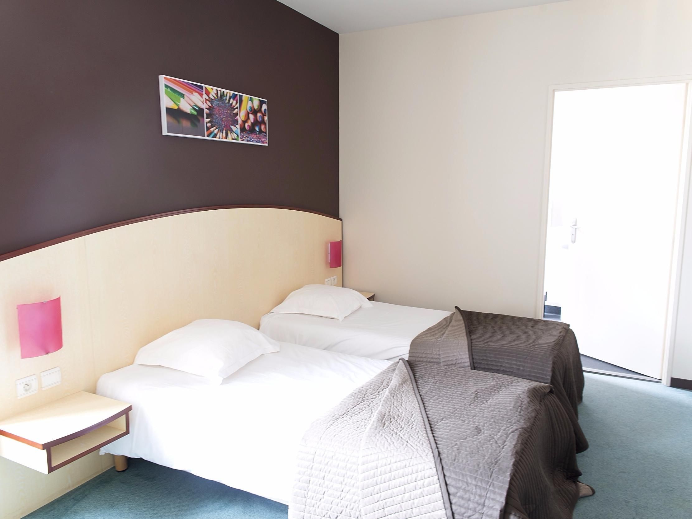 A hotel room with a bed, bedside tables, a wall-mounted picture, and a door.