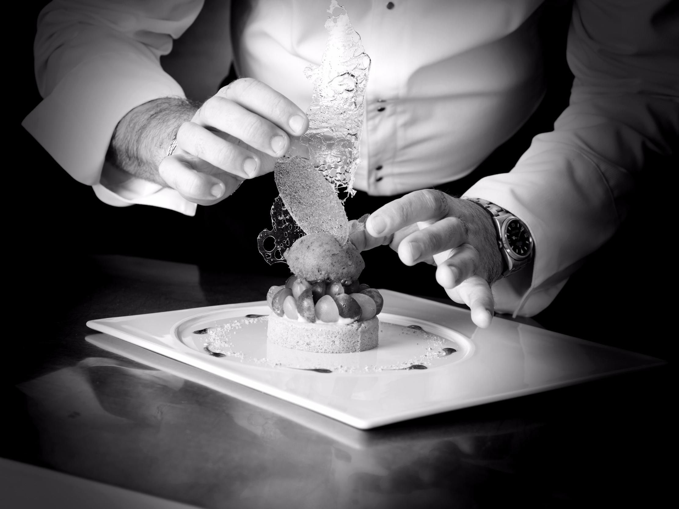 A person in a white shirt and watch, slicing a cake with a decorative top.