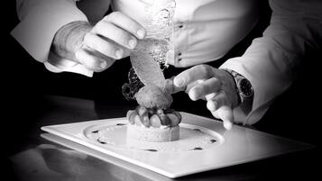 A person in a white shirt and watch, slicing a cake with a decorative top.
