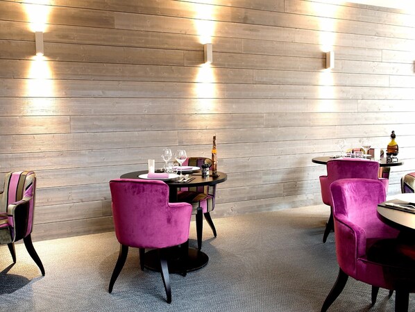 Un comedor con paneles de madera, mesas redondas y sillas moradas.